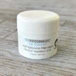 Closed jar of Dermotechnology La Solution Acid Hyaluronic Filler cream on a wooden texture background