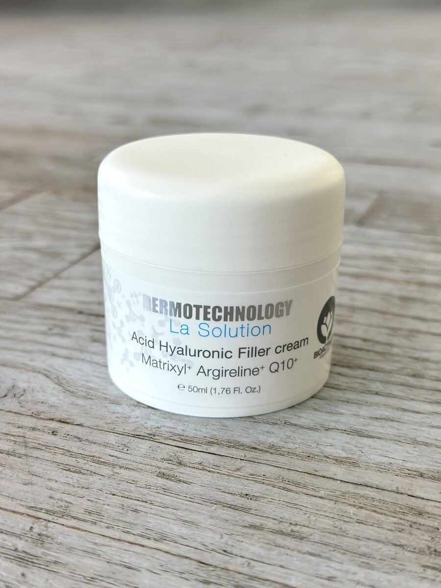 Closed jar of Dermotechnology La Solution Acid Hyaluronic Filler cream on a wooden texture background