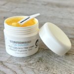 Open jar of Dermotechnology La Solution Acid Hyaluronic Filler cream with a spatula on wooden surface