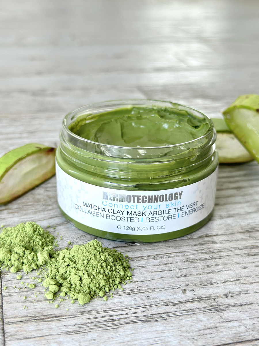 Open jar of Dermotechnology Matcha Clay Mask with matcha powder and aloe slices on a wooden background