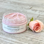 Open jar of Dermotechnology Bio Active Rose Clay Mask with a delicate pink rose on wooden background
